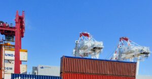 Colorful cargo containers stacked at a busy shipping port under a clear blue sky.